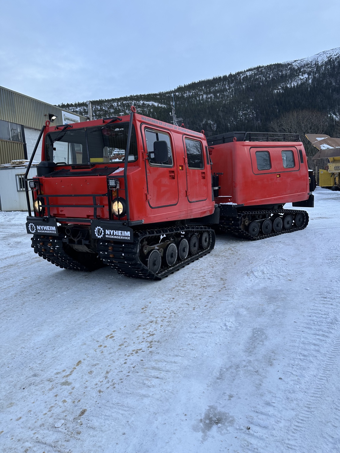 Komplett rød Hägglunds BV206 med framvogn og passasjerbakvogn.